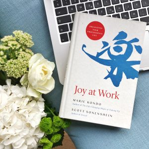 the book joy at work positioned on a labtop next to flowers